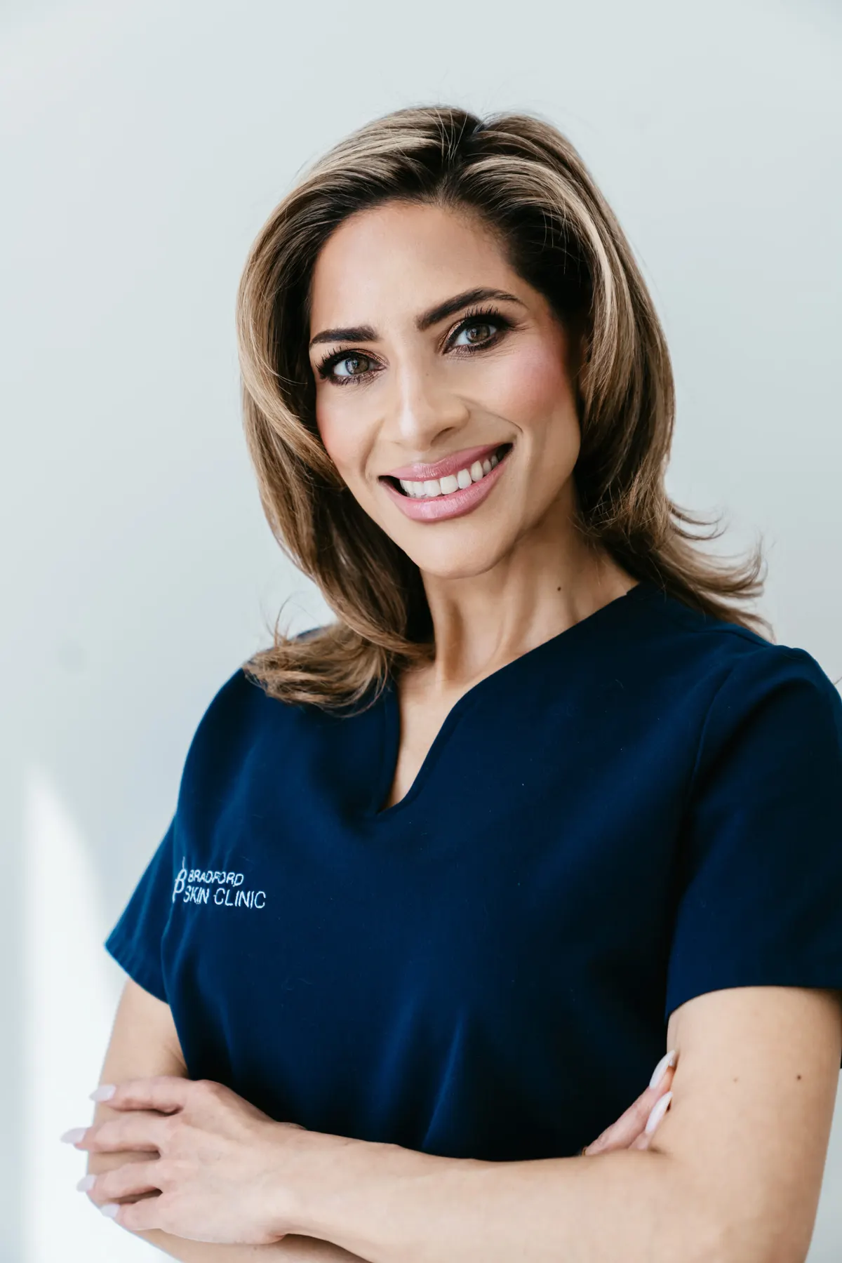 A member of the clinic team in Bradford Skin Clinic navy scrubs photographed against a plain pale background.