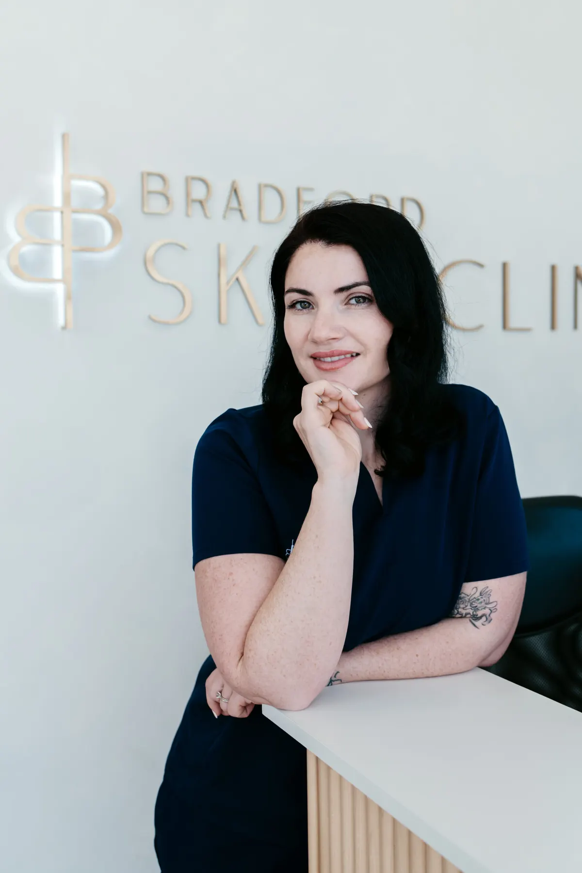 Alex Dinovich in navy Bradford Skin Clinic scrubs at the clinic reception desk