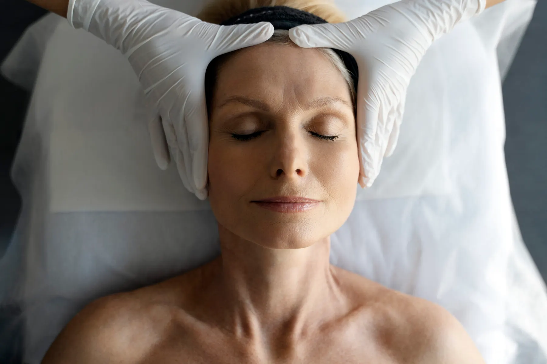 A gloved clinician examining a client's skin closely during a consultation