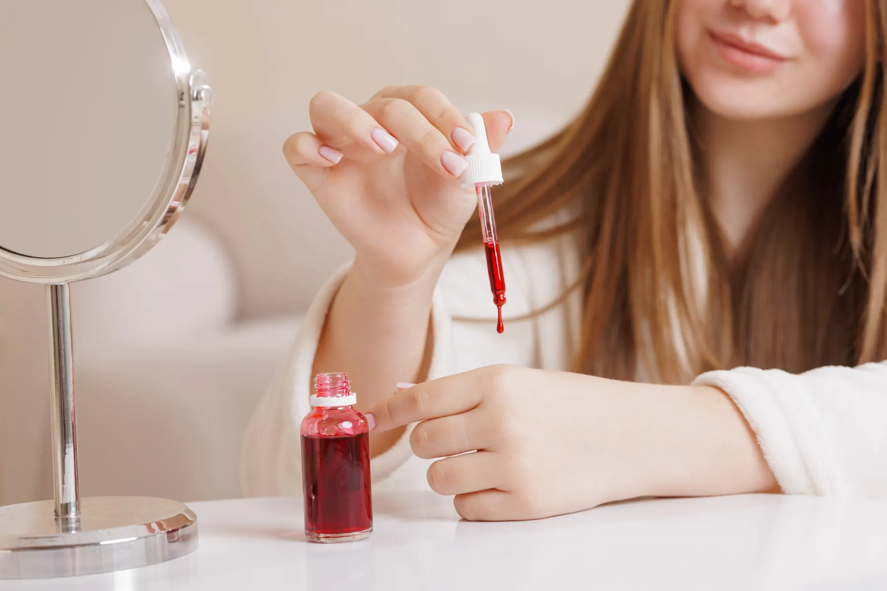A young woman applying a hydrating facial serum in a bright setting