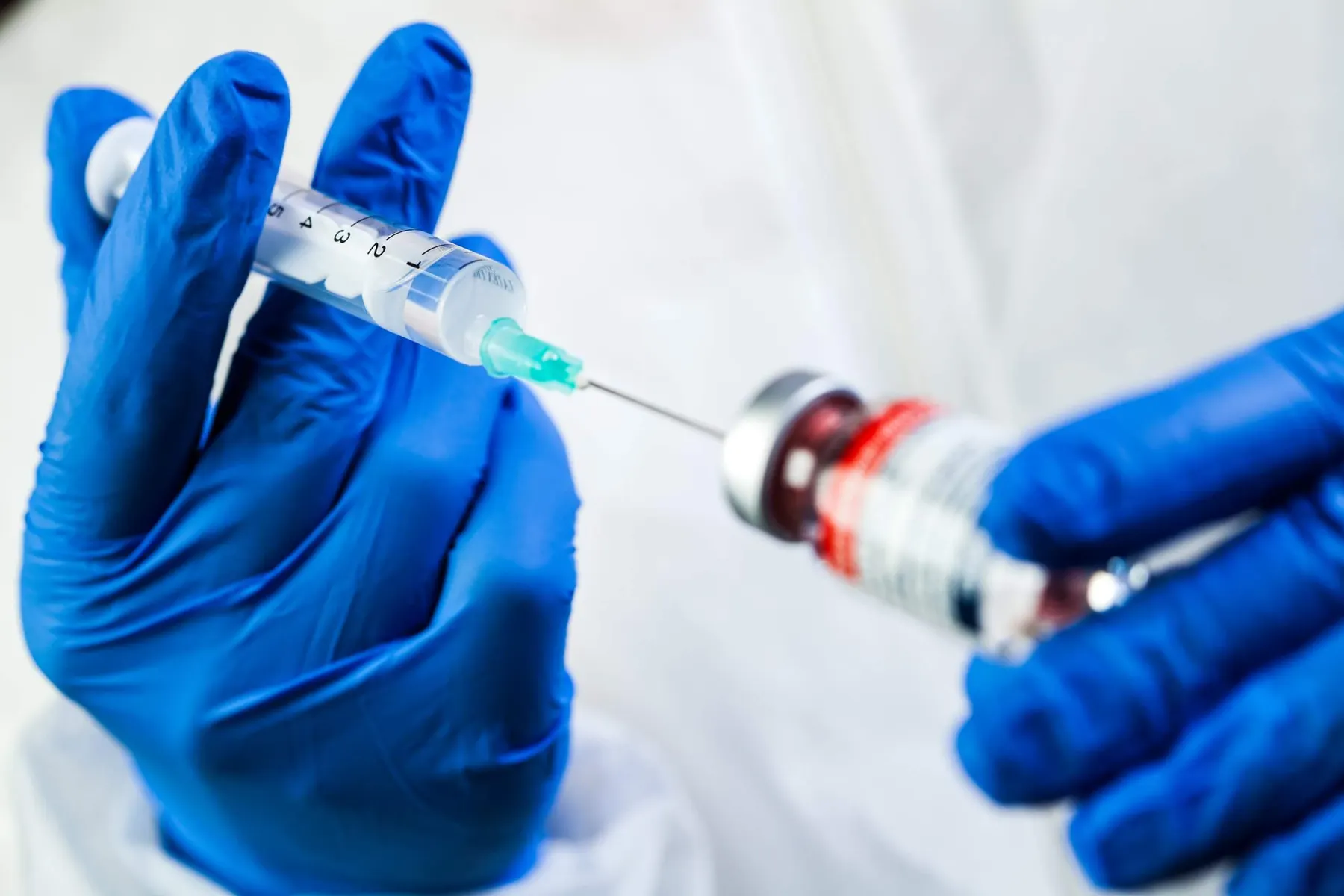 Blue gloved hands drawing up a syringe from a vial