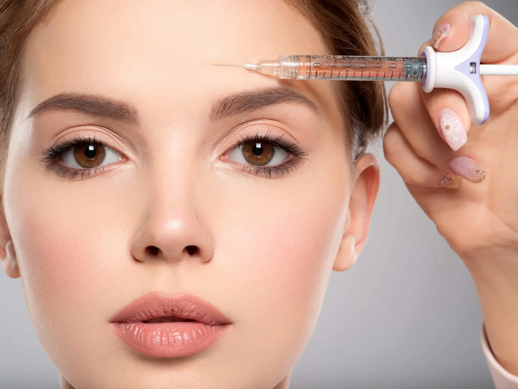 White-gloved hands holding a fine syringe against the brow of a woman looking at the camera.