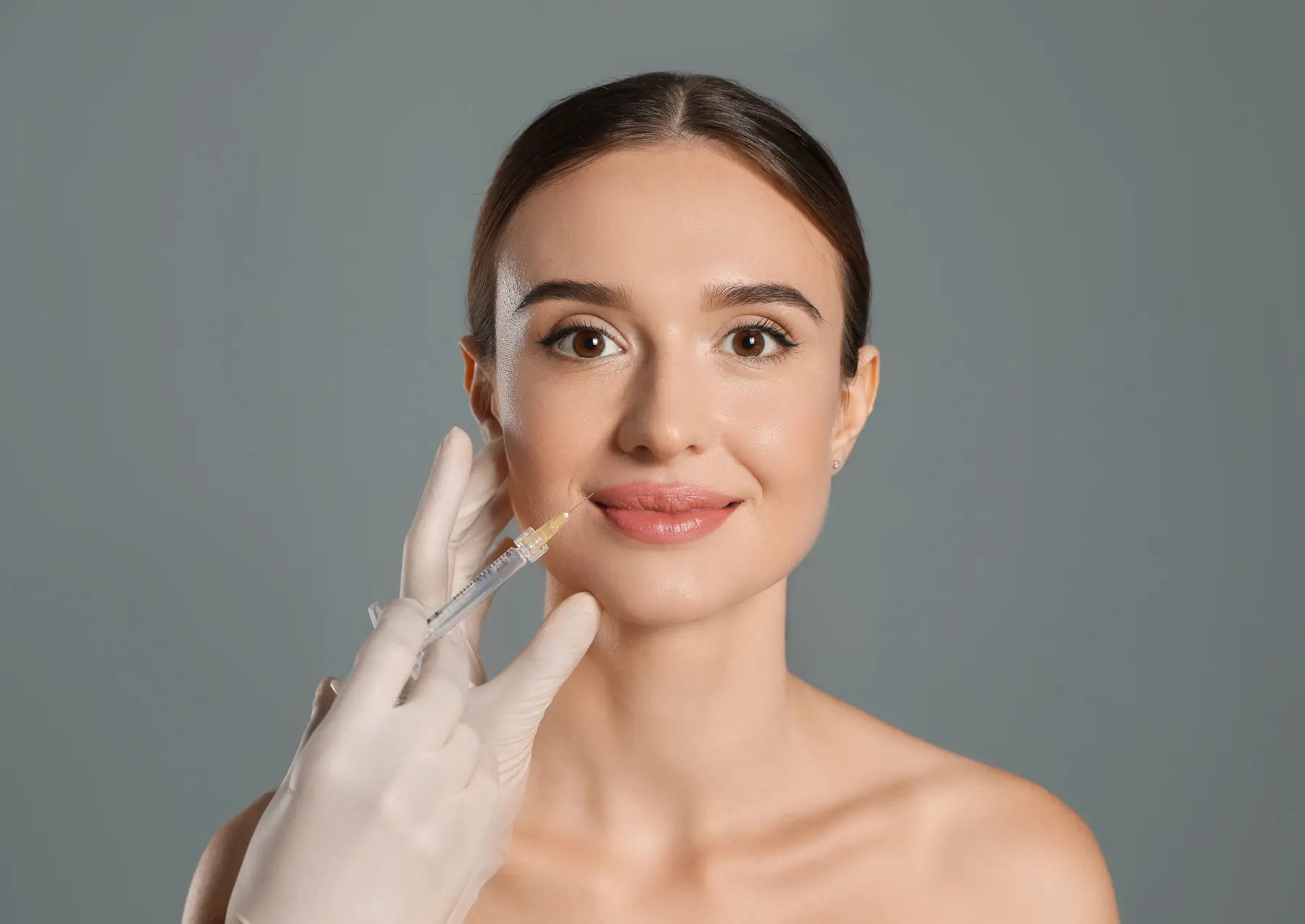 A gloved hand injecting dermal filler into a client's lip