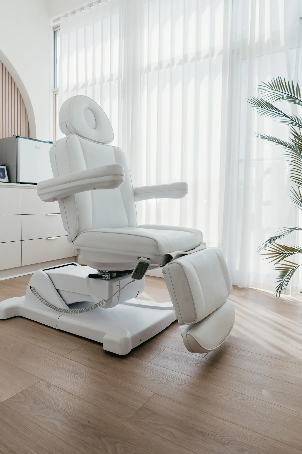 A white reclining treatment chair in a bright, empty treatment room