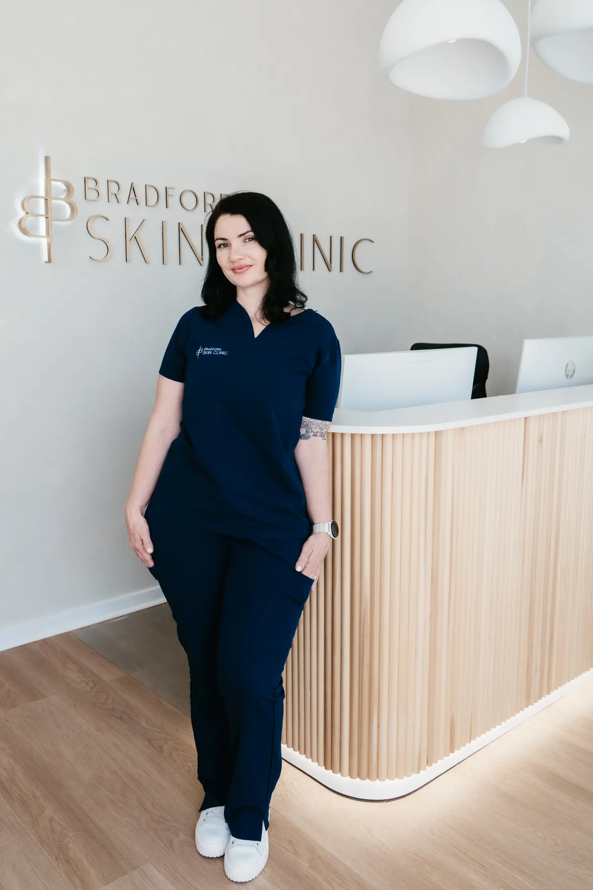 Alex Dinovich in navy scrubs at the reception desk of Bradford Skin Clinic